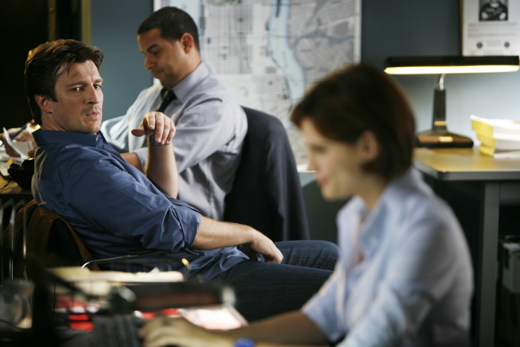 Castle (Nathan Fillion) observe Beckett (Stana Katic), concentrée sur son travail. 